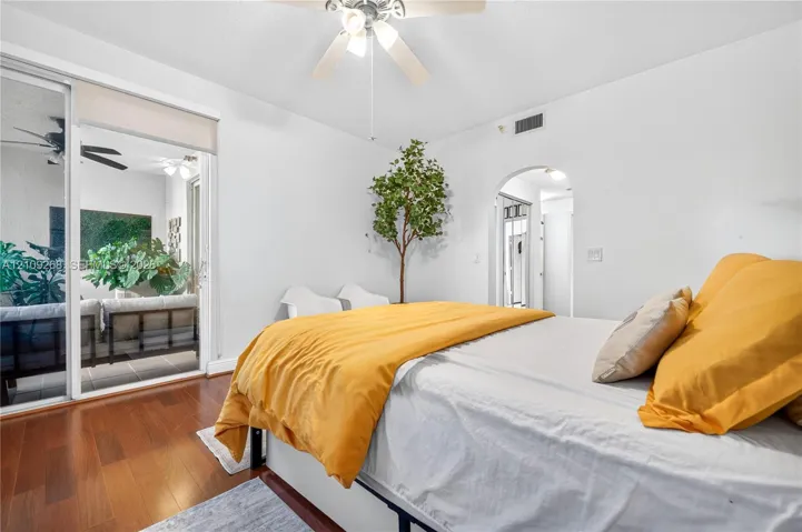 Wood-finish flooring, ceiling fan with integrated lighting, sliding glass door, and arched doorway