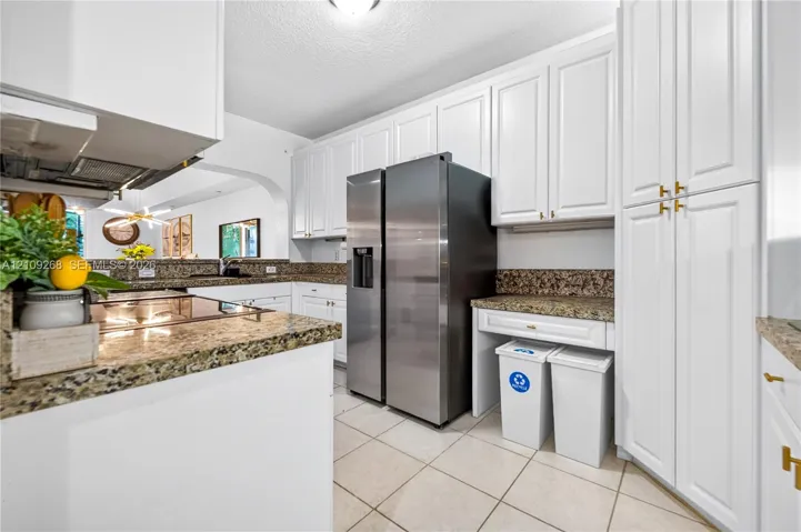 Kitchen featuring white shaker-style cabinetry, stone-finish countertops, stainless steel side-by-side refrigerator, tile flooring, and integrated built-in storage