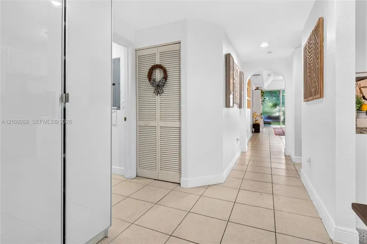 Hallway featuring neutral tile flooring, arched passageway, and louvered bi-fold closet doors