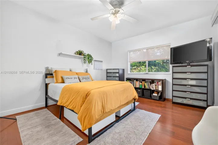 Room featuring wood-finish flooring, a ceiling fan with integrated lighting, and a window with a roller shade