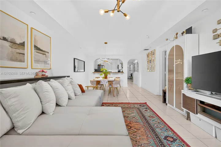 Tray ceiling, neutral tile flooring, modern multi-arm chandelier lighting, and arched architectural wall opening