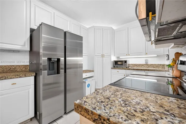 Kitchen featuring white shaker-style cabinetry, stone-finish countertops, stainless steel side-by-side refrigerator, flat-surface cooktop, and under-cabinet task lighting