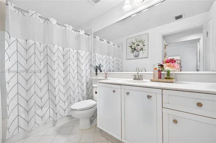 Bathroom featuring white cabinetry, an integrated basin, a large wall-mounted mirror, and tile flooring