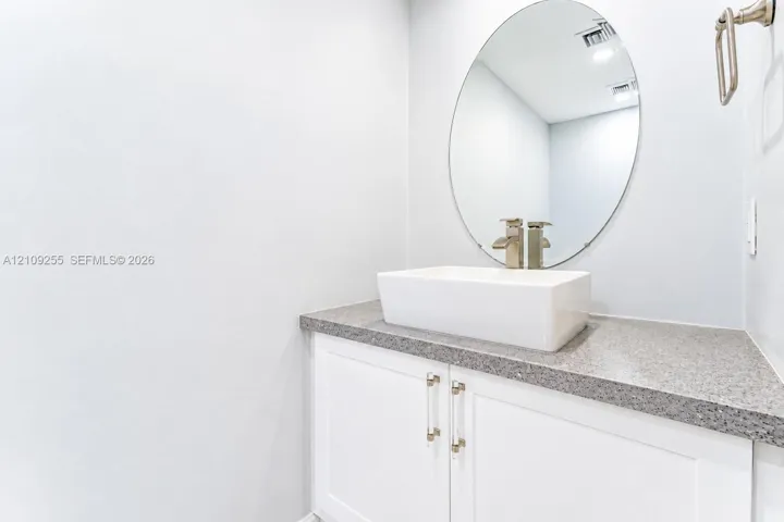 White vanity featuring a rectangular vessel sink, stone-finish countertop, oval mirror, and metallic hardware