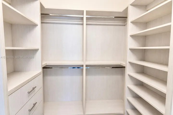 Custom walk-in closet featuring light-toned cabinetry, built-in shelving units, integrated hanging rods, and stacked storage drawers with metallic hardware