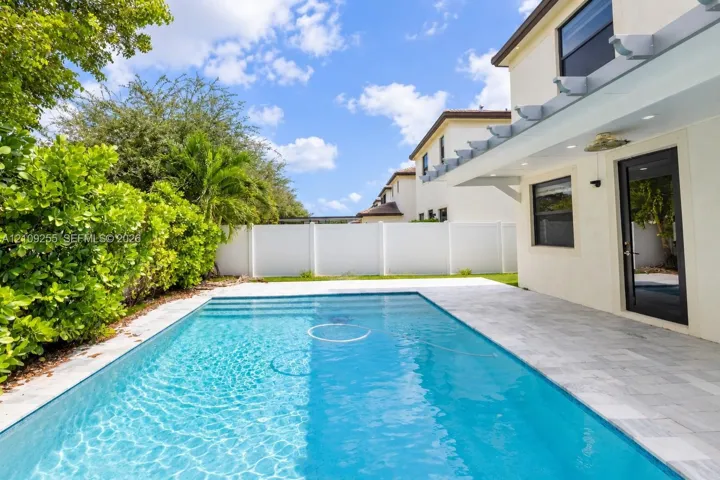 In-ground swimming pool featuring a tiled patio, white vinyl perimeter fencing, and an overhead trellis