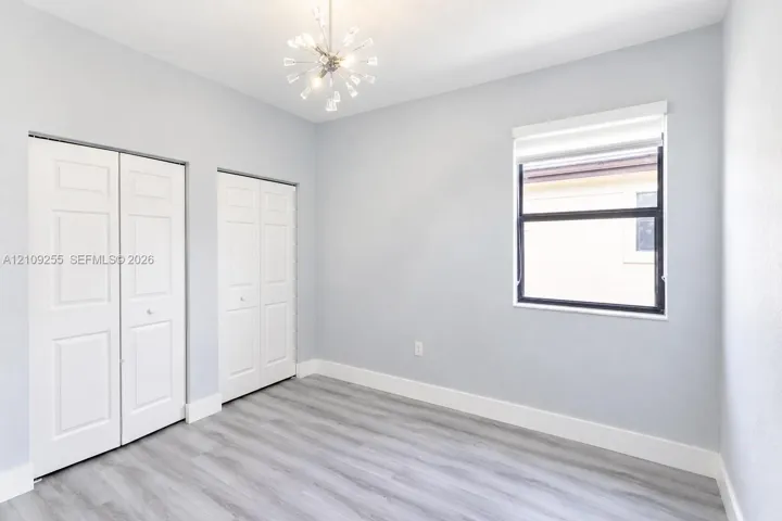 Wood-finish flooring, dual-panel closet doors, single-light window with shade, and starburst-style ceiling light fixture