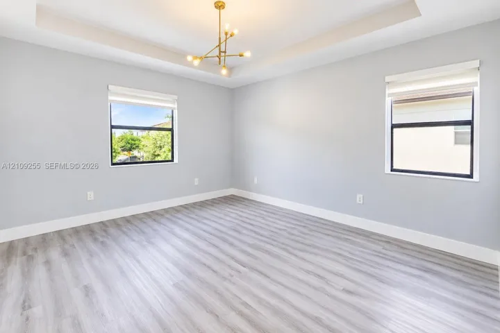 Room featuring a tray ceiling, wood-finish flooring, gold-tone multi-arm chandelier, and large windows with integrated roller shades