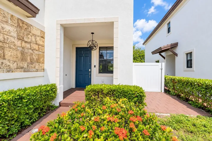 Stucco exterior featuring stone-veneer accents, covered entryway with a circular pendant light, paneled blue front door, and brick-patterned paved walkway