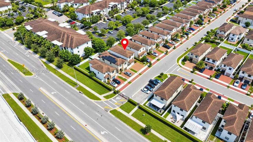 Aerial perspective of residential property featuring a multi-story layout, roof-mounted solar panel array, attached garage, paved driveway, and curated landscaping