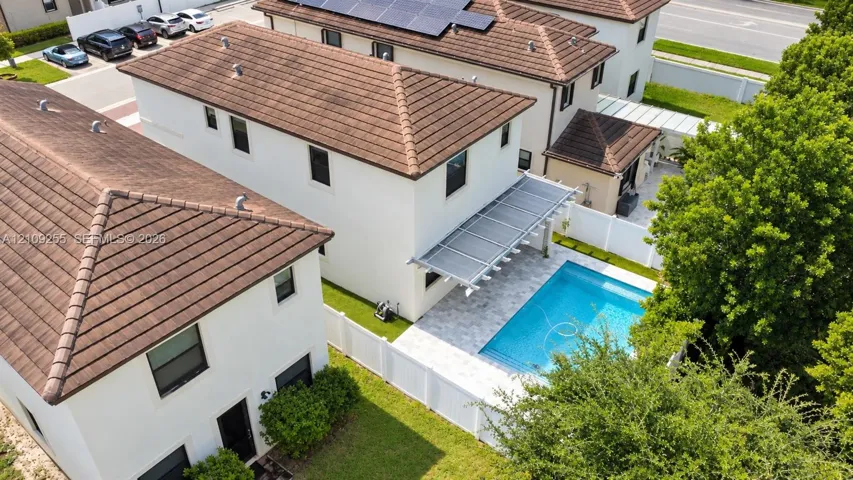Exterior featuring a tile roof with installed solar panels, a backyard swimming pool, stone-finish patio, and white vinyl perimeter fencing