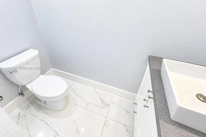 Bathroom featuring large-format tile flooring with marble-finish veining, white cabinetry, a neutral stone-finish countertop, and a rectangular vessel sink