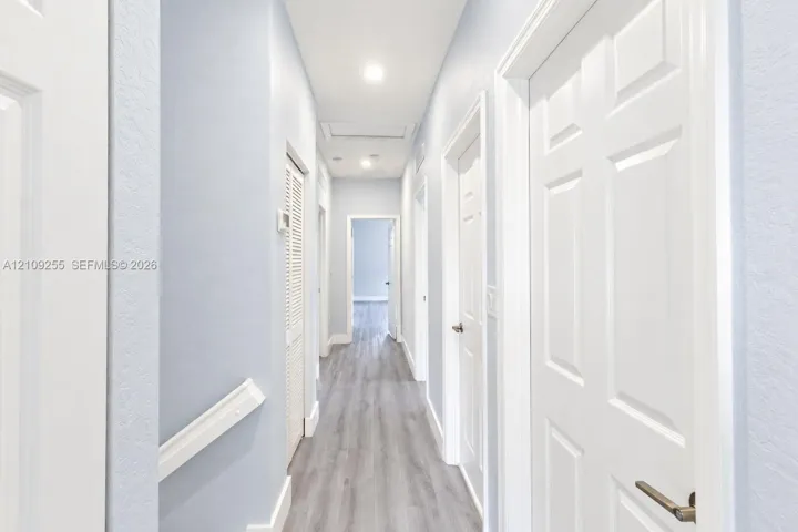 Hallway featuring wood-finish flooring, white panel doors, recessed ceiling lighting, and louvered closet cabinetry