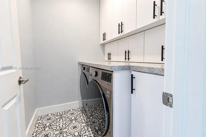 Utility space featuring white shaker-style cabinetry, matte black hardware, stone-finish countertops, and patterned tile flooring
