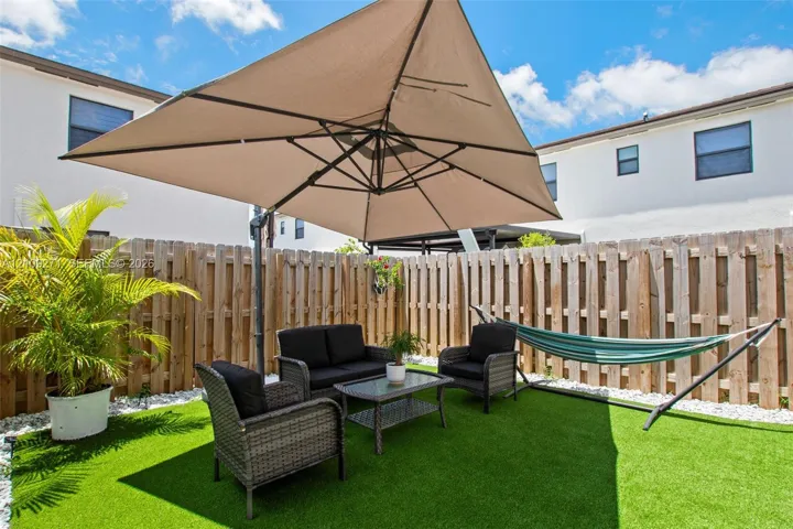 Fenced backyard featuring synthetic turf, light-colored stone edging, and vertical wood-slat privacy fencing