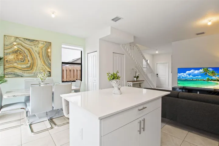 Kitchen featuring a central island with a quartz countertop, white cabinetry, light tile flooring, and a staircase with a white wood balustrade