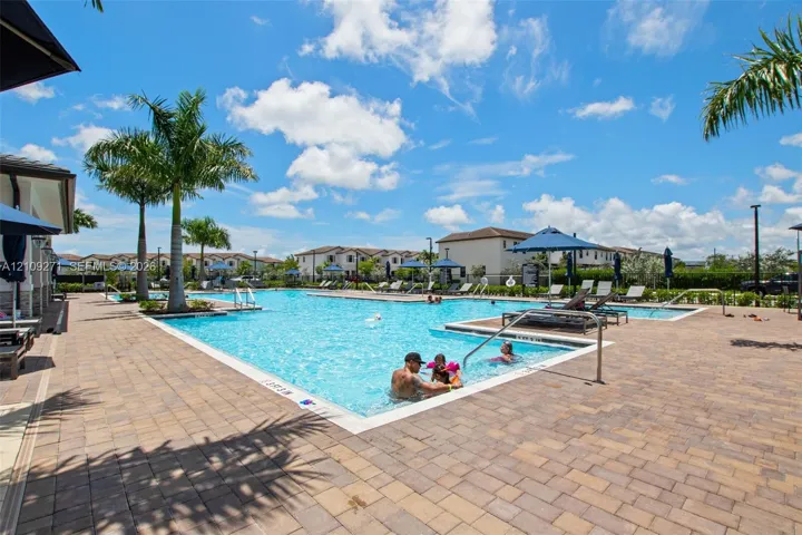 Outdoor pool area featuring a paved deck, surrounding palm trees, and metal handrails