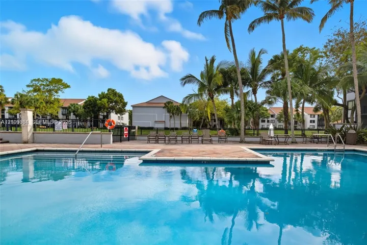 Outdoor swimming pool featuring a paved pool deck, perimeter fencing, and mature palm trees