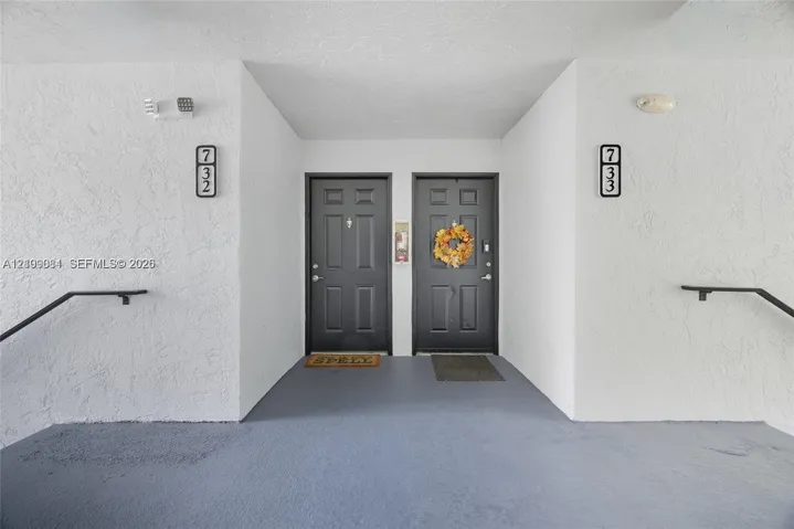 Exterior entry featuring dual dark-toned doors, textured white wall surfaces, and black metal handrails