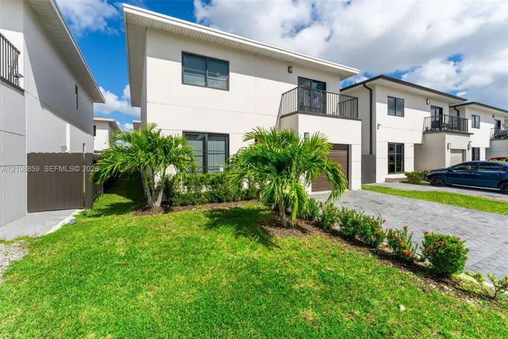 Two-story modern exterior featuring smooth stucco siding, a second-level balcony with metal railing, an integrated garage with wood-finish door, and paver driveway