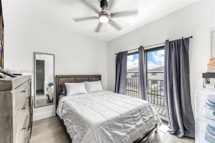 Room featuring wood-finish flooring, a ceiling fan with integrated lighting, and a sliding glass door providing access to a balcony with metal railing