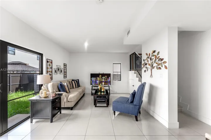 Living area featuring large-format tile flooring, sliding glass door access to the rear exterior, and an open staircase with a metal railing