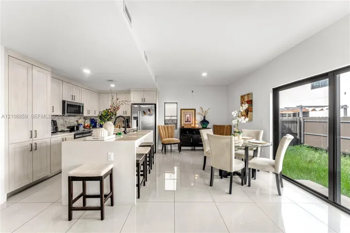 Kitchen featuring light wood-finish cabinetry, a large central island with solid surface countertop, stainless steel appliances, large-format tile flooring, and sliding glass doors leading to the exterior