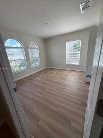 Room featuring wood-finish flooring, two arched windows, and a standard rectangular window