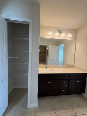 Bathroom featuring a vanity with dark-finish cabinetry, a solid-surface countertop, an integrated sink, a large wall-mounted mirror, and a built-in closet with tiered shelving