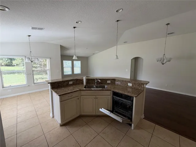 Kitchen featuring a center island with a stone-finish countertop, stainless steel dual-basin sink, integrated dishwasher, and tile flooring, highlighted by vaulted ceilings and multiple pendant light fixtures