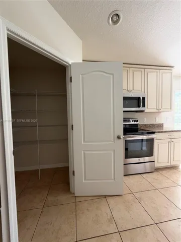 Kitchen pantry featuring built-in wire shelving, off-white cabinetry, stainless steel appliances, stone-look countertops, and tile flooring