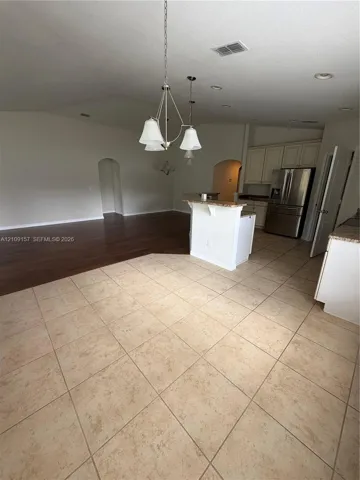 Kitchen featuring light-toned cabinetry, stone-finish countertops, stainless steel refrigerator, tile flooring, and a multi-light pendant fixture