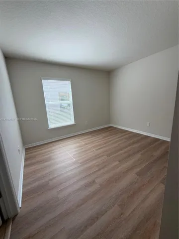 Neutral wall paint, wood-finish flooring, and a window featuring integrated blinds