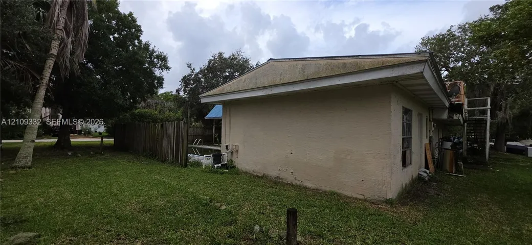 Stucco exterior, in-ground swimming pool, wood-plank fencing, and mature trees on the lot