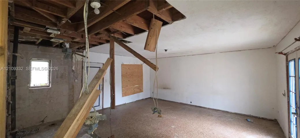 Interior space featuring exposed wooden ceiling rafters, white wall finish, single-pane window, and glass-paneled double doors