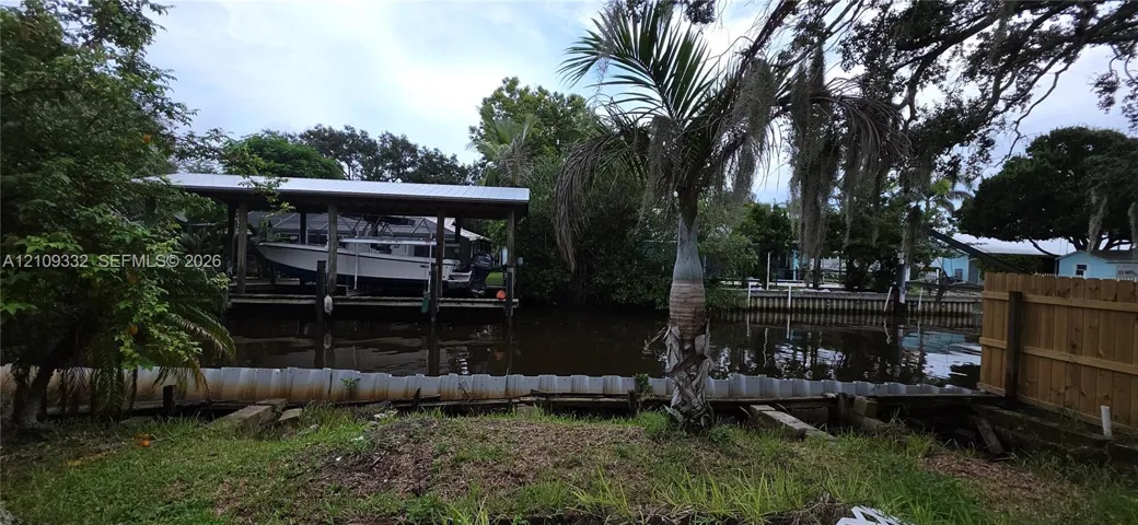 Waterfront property featuring a private covered boat lift, bulkhead seawall, and mature tropical landscaping