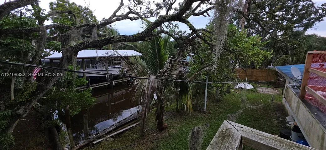 Canal-front property featuring a private boat dock, mature oak trees, tropical landscaping, and a fenced perimeter