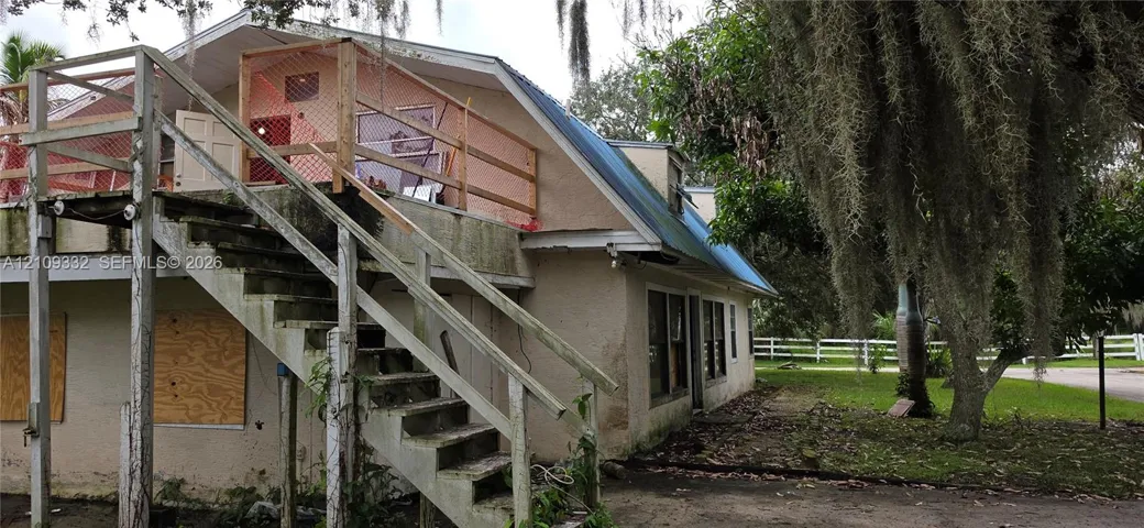 Exterior featuring a stilt-style structure with an elevated wooden deck and exterior staircase, metal roof, and surrounding mature trees
