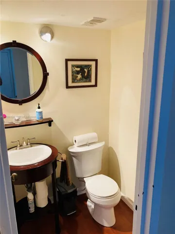 Console-style wood vanity featuring an integrated round mirror, porcelain basin, polished metal hardware, and wood-finish flooring