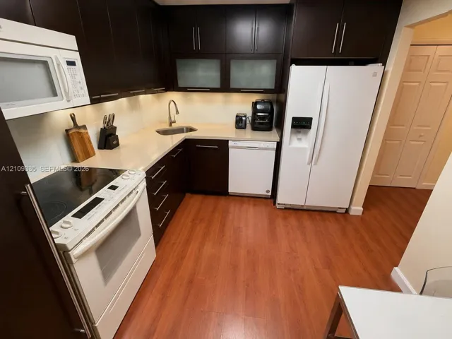 Kitchen featuring dark wood-finish cabinetry, solid surface countertops, glass-paneled upper cabinets, and wood-finish flooring