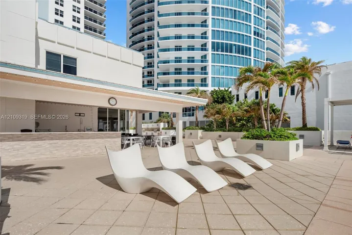 Outdoor terrace featuring a covered bar area with stone-tile facade, concrete pavers, and integrated palm tree planters