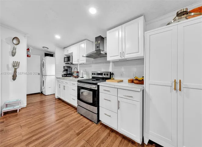 Kitchen featuring white cabinetry, stainless steel range with overhead hood, subway tile backsplash, wood-finish flooring, and built-in floor-to-ceiling storage