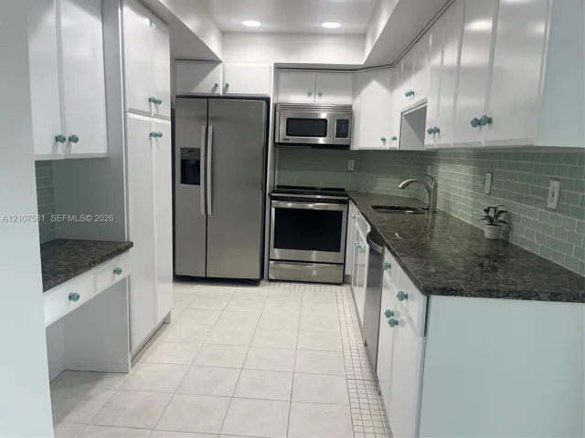 White cabinetry, dark stone countertops, stainless steel appliances, light tile flooring, and a green subway tile backsplash