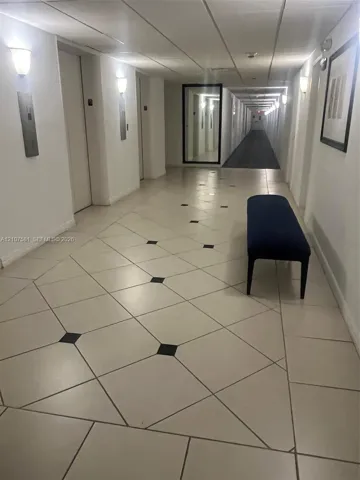 Hallway featuring diagonal tile flooring with black accent squares, wall-mounted sconce lighting, and a full-length mirror
