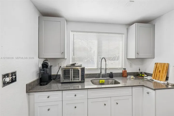 Kitchen featuring Shaker-style cabinetry, solid-surface countertops, undermount stainless steel sink, and high-arc pull-down faucet