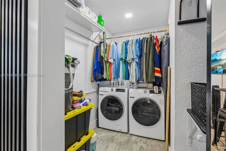 Laundry area featuring white front-loading washer and dryer, integrated overhead shelving, a dedicated garment rod, and tile flooring