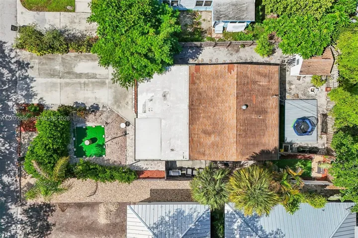 Aerial view of property featuring a multi-section roofline, expansive concrete driveway, stone-covered grounds, and mature landscaping