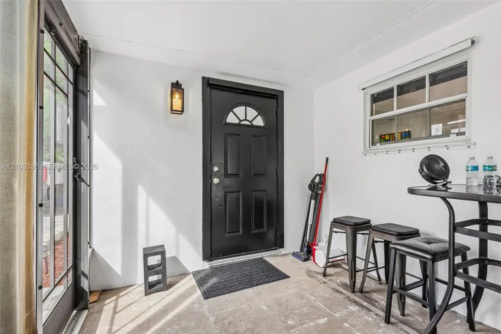 Covered entry featuring a black multi-panel door with arched window detail, a wall-mounted exterior lantern, and a multi-pane horizontal window