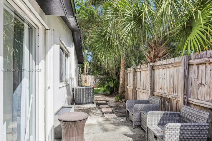 Side patio featuring concrete pavers, wood-panel fencing, mature palm trees, and sliding glass door access