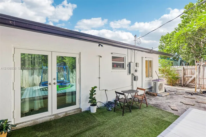 Exterior wall featuring white smooth stucco finish, double French doors with glass panes, and a dedicated outdoor heating and cooling unit